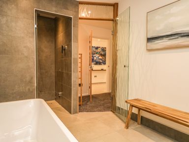 A bathroom with a bathtub wooden bench glass door open to a carpeted hallway at Kessock in Bowness-On-Windermere