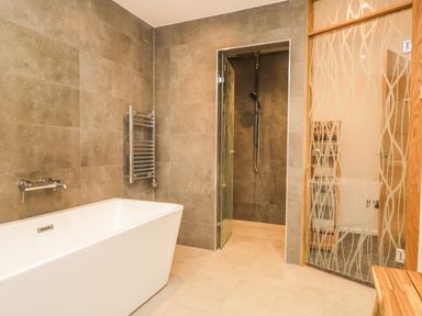A bathroom with a freestanding bathtub shower area with glass door and glass door with wooden frame at Kessock in Bowness-On-Windermere