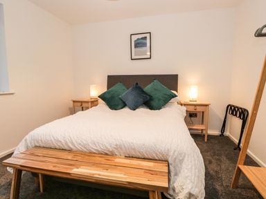 A bedroom with a bed with white bedding and three pillows two bedside tables with lamps and a wooden bench at the foot of the bed at Kessock in Bowness-On-Windermere
