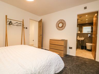 A bedroom with a bed a wooden dresser a round mirror a clothes rack and an open door leading to a bathroom at Kessock in Bowness-On-Windermere