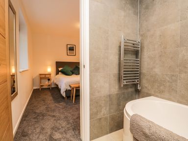 A bedroom with a bed and bedside table adjacent to a bathroom with a bathtub and towel heater at Kessock in Bowness-On-Windermere