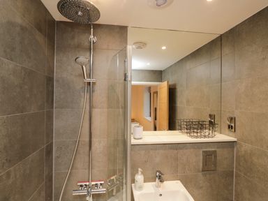 A bathroom with a shower area a sink a mirror and a metal basket at Kessock in Bowness-On-Windermere