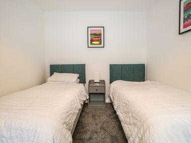 A bedroom with two single beds separated by a nightstand with a lamp and two framed pictures on the wall at Kessock in Bowness-On-Windermere