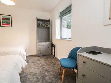 A bedroom with two beds a blue chair a grey dresser and a small wardrobe with hangers at Kessock in Bowness-On-Windermere