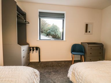 A bedroom with two beds gray carpet blue chair gray drawers and a window at Kessock in Bowness-On-Windermere