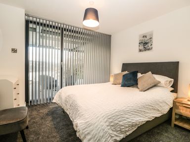 A bedroom with a large bed and pillows next to a sliding glass door with vertical blinds at Kessock in Bowness-On-Windermere