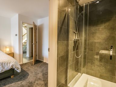 A bedroom with an open door leading to a hallway next to a shower cubicle with glass doors and tiled walls at Kessock in Bowness-On-Windermere