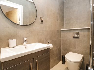A bathroom with a sink and mirror above it and a toilet with a toilet brush beside it at Kessock in Bowness-On-Windermere