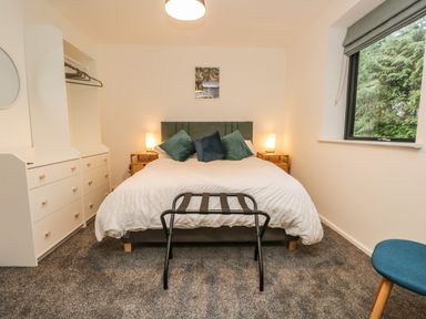 A bedroom with a double bed, bedside tables with lamps, a window, a luggage rack, and a chest of drawers at Kessock in Bowness-On-Windermere