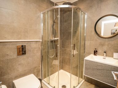 A bathroom with a glass shower enclosure a toilet a sink with soap dispenser and an oval mirror at Kessock in Bowness-On-Windermere