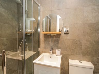 A bathroom with a shower cabin, sink, round mirror, and toilet at Kessock in Bowness-On-Windermere
