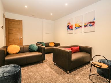 A lounge area with three brown sofas with colorful cushions a small round side table a remote control and abstract artwork on the wall at Kessock in Bowness-On-Windermere