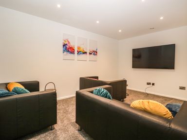A room with three black sofas facing a wall-mounted TV and abstract artwork on the wall at Kessock in Bowness-On-Windermere