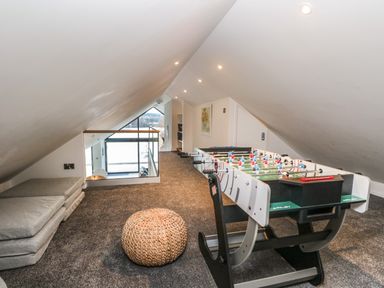 An attic room with a foosball table cushions on the floor and a woven ottoman at Kessock in Bowness-On-Windermere