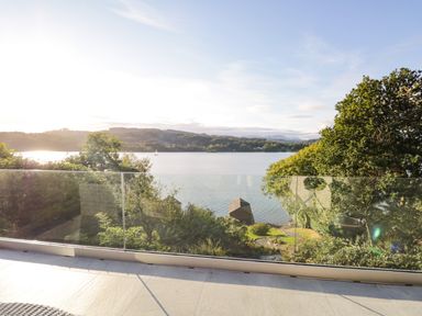 A balcony with glass railing overlooking a lake with trees and hills in the background at Kessock in Bowness-On-Windermere