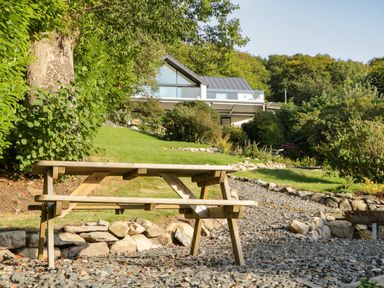A wooden picnic table on gravel with a modern house and garden in the background at Kessock in Bowness-On-Windermere