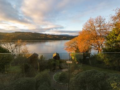 A lake view with trees and garden behind a glass railing at Kessock in Bowness-On-Windermere