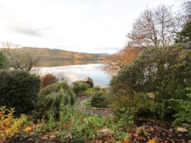 A garden with shrubs and a pathway leading to a boathouse on the shore of a lake at Kessock in Bowness-On-Windermere