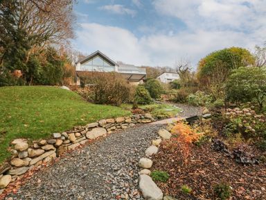 A gravel path leading to a modern house surrounded by grass bushes and trees at Kessock in Bowness-On-Windermere