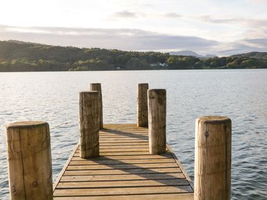A wooden dock extending over a lake with trees and hills in the background at Kessock in Bowness-On-Windermere