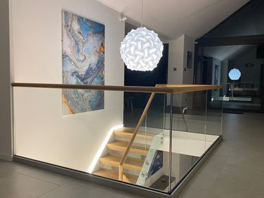 A staircase with wooden handrails and glass panels a white spherical pendant light and abstract wall art at Kessock in Bowness-On-Windermere
