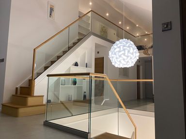 An interior view of a modern staircase with glass railings wooden handrails built-in shelves with decorative vases and a hanging spherical white light fixture at Kessock in Bowness-On-Windermere
