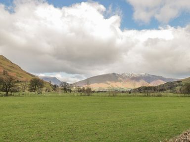 A green field with trees and mountains in the background under a cloudy sky in Keswick