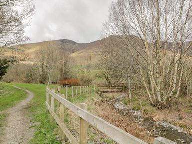 A dirt path with a wooden fence beside a small stream and leafless trees at Sparrow Cottage in Keswick