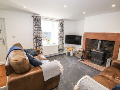 A living room with leather sofas curtains a window a wall mounted tv and a fireplace at Sparrow Cottage in Keswick