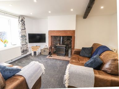 A living room with brown leather sofas a fireplace and a wall-mounted TV at Sparrow Cottage in Keswick