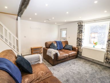 A living room with brown leather sofas blue and gray cushions a small wooden table and a window with patterned curtains at Sparrow Cottage in Keswick