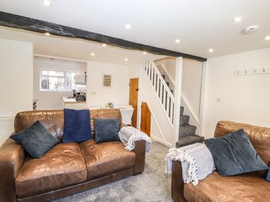 A living room with two brown sofas blue cushions and a view of a staircase and kitchen at Sparrow Cottage in Keswick