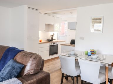 A kitchen and dining area with white cabinets a brown sofa with blue cushions and a dining table with four white chairs at Sparrow Cottage in Keswick