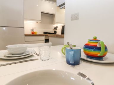 A kitchen with dishes and glasses on a white table and a rainbow teapot at Sparrow Cottage in Keswick