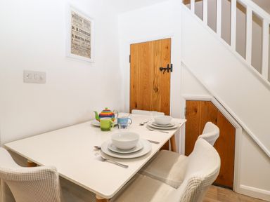 A dining table with dishware and a teapot next to wooden doors under stairs at Sparrow Cottage in Keswick