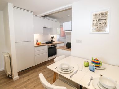 A kitchen with white cabinets wooden countertops dining table set with dishes cups and cutlery and a colorful teapot at Sparrow Cottage in Keswick
