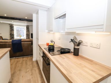 A kitchen with wooden countertops cooking utensils and a stovetop next to a living area with a brown sofa and a window at Sparrow Cottage in Keswick