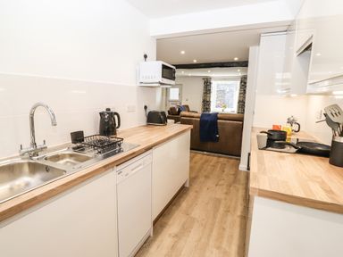 A kitchen with wooden countertops a sink kettle toaster microwave and living area with brown sofas at Sparrow Cottage in Keswick