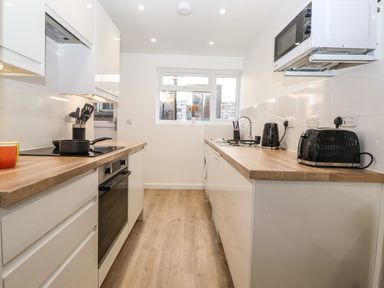 A galley kitchen with wooden countertops black toaster kettle and microwave at Sparrow Cottage in Keswick