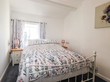 A bedroom with a white metal bed frame floral bedding two bedside tables with lamps at Sparrow Cottage in Keswick