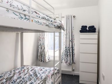 A bedroom with a bunk bed and a tall white dresser with folded towels on top at Sparrow Cottage in Keswick