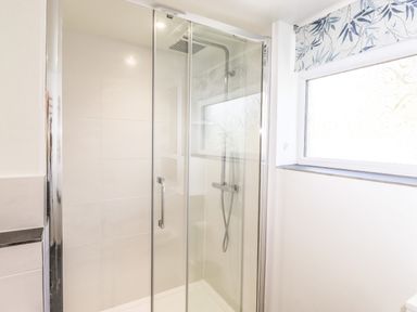 A bathroom with a glass shower enclosure and a window with a patterned blind at Sparrow Cottage in Keswick