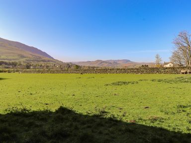 A green field with sheep and stone wall with hills in the background at Sparrow Cottage in Keswick