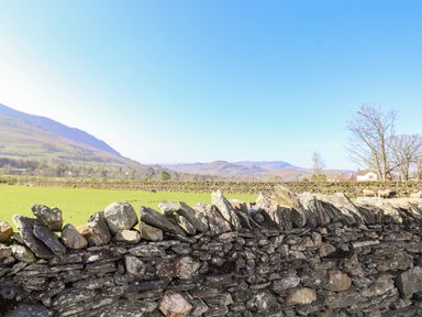 A stone wall in front of a grassy field with mountains in the background at Sparrow Cottage in Keswick