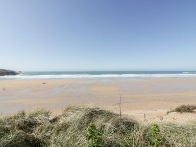 A sandy beach with waves and grassy dunes in the foreground at Fistral Apres Surf in Newquay