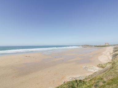 A wide sandy beach with ocean waves and a grassy hill with a building in the distance at Fistral Apres Surf in Newquay
