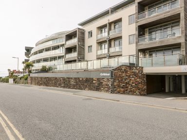 A street view of a multi-story modern building with balconies and a stone wall with Cribbar sign at Fistral Apres Surf in Newquay