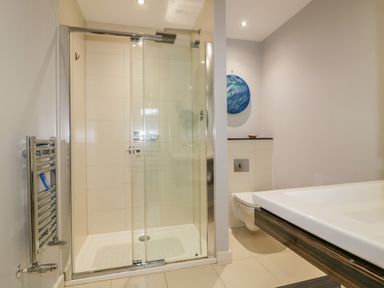 A bathroom with a glass shower enclosure a wall-mounted toilet and a sink at Fistral Apres Surf in Newquay