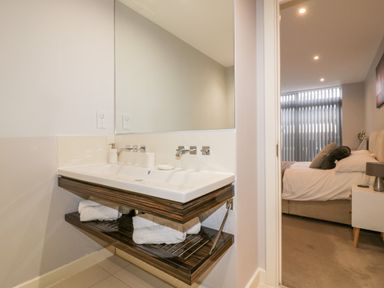 A bathroom sink with towels on a wooden shelf and a view of a bedroom with a bed at Fistral Apres Surf in Newquay