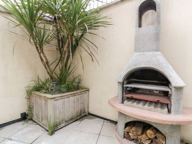 An outdoor corner with a wooden planter containing a plant and a concrete barbecue grill with firewood underneath at Fistral Apres Surf in Newquay